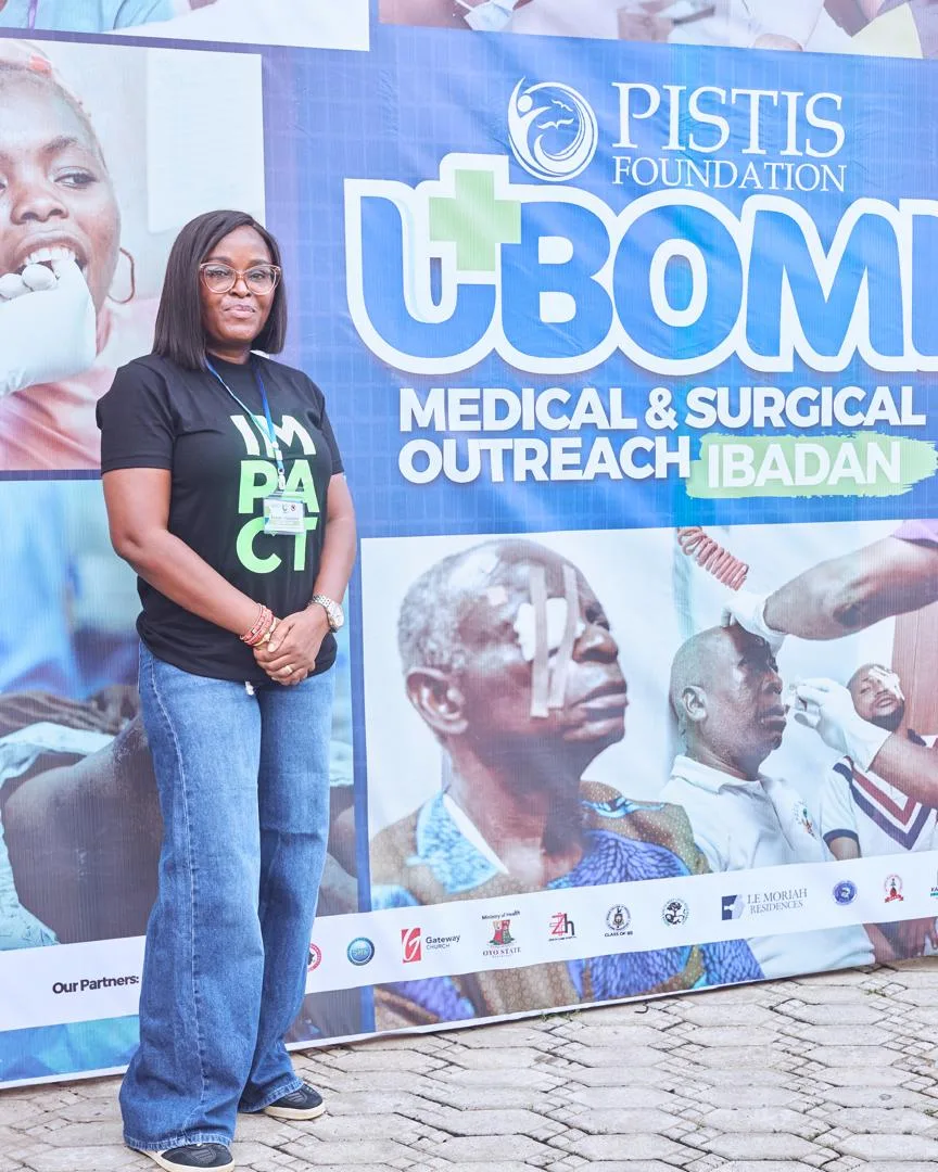Sowari Akosionu beside a UBOMI Medical and Surgical Outreach Ibadan banner